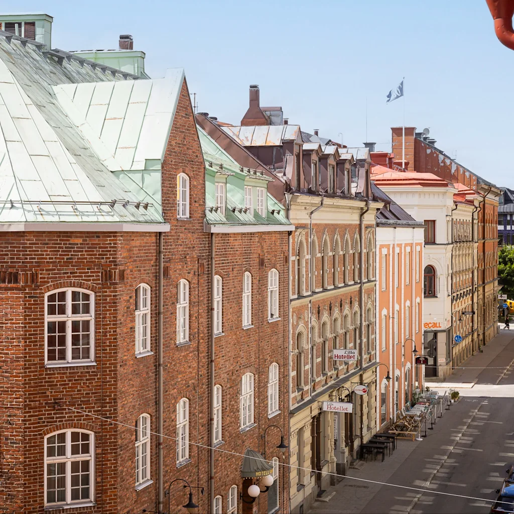Viehättävä katunäkymä Sundsvallissa historiallisilla rakennuksilla, joista osassa on vihreät katot, ja pysäköityjä autoja tien varrella. Hotellikyltti näkyy.