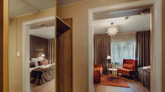A cozy hotel room with a warm ambiance, viewed through a doorway, featuring elegant furniture and decorative lighting.