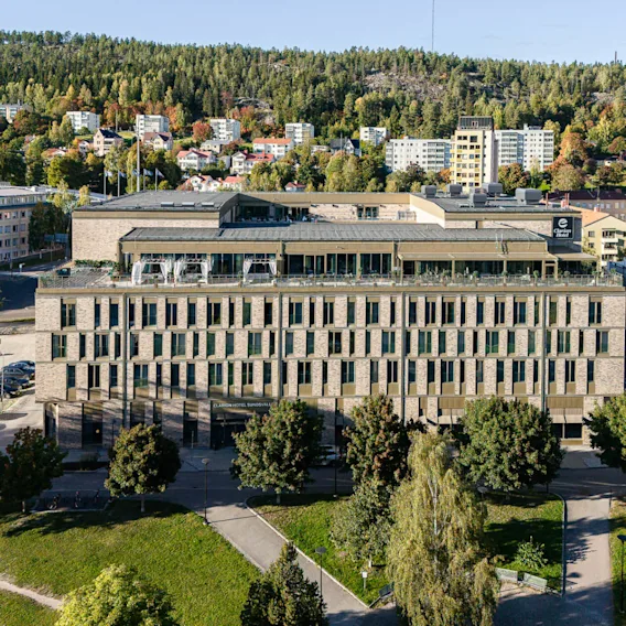 A large, rectangular hotel stands in a green suburban area with trees and low-rise buildings. Visible text: "CLARION HOTEL SUNDSVALL" and "e Clarion Hotel."