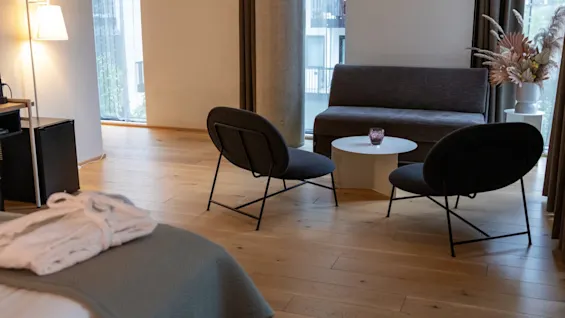 Sittegruppe på hotellrom med sofa, to lenestoler og salongbord, med en seng i forgrunnen