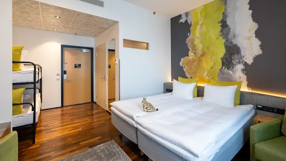 A modern hotel room with a large bed, a bunk bed, and a vibrant abstract mural on the wall.