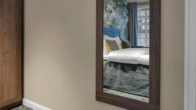 A framed mirror view into a hotel room, with green floral accents in both rooms.