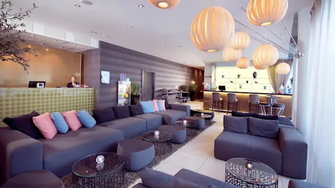 A modern hotel lobby with comfortable seating, hanging spherical lamps, and a reception desk, providing a welcoming ambiance for guests.