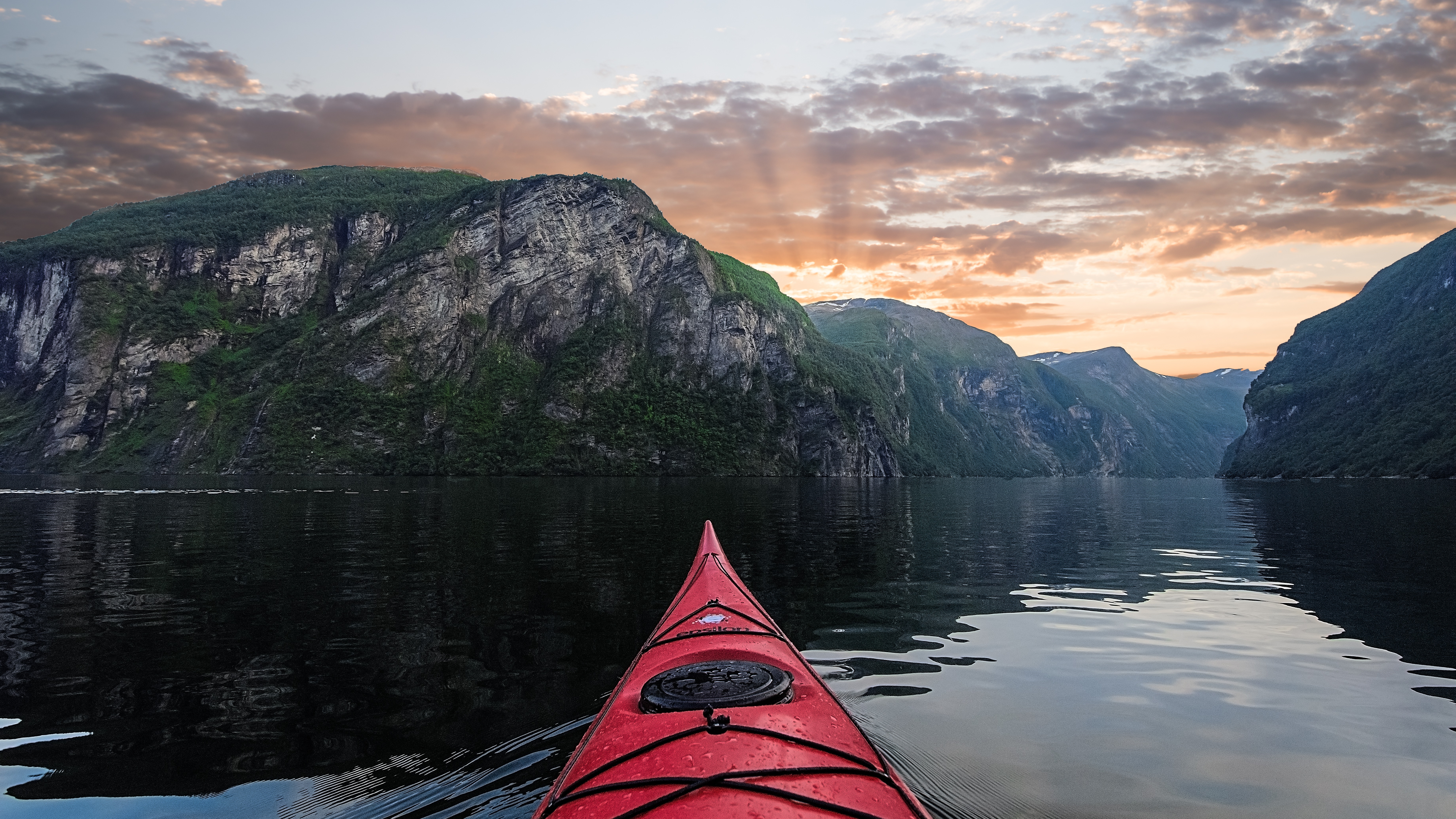 Red kayak gliding across fjord waters with steep Norwegian mountains at sunset