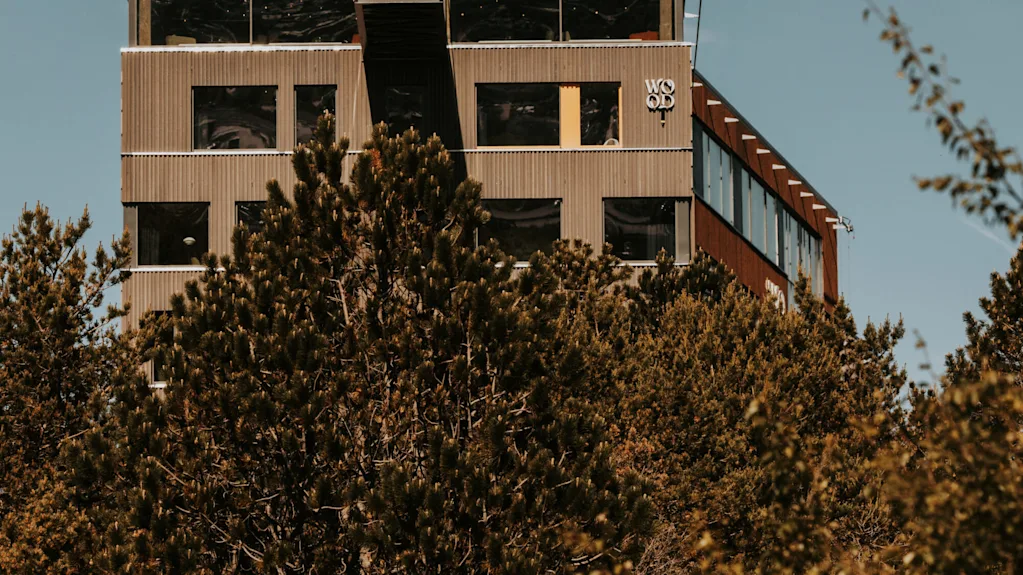 A modern building with "WOOD" text visible, surrounded by green trees against a clear blue sky.