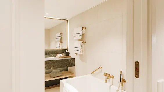 Ett ljust modernt hotellbadrum med ett vitt badkar, gulddetaljer och en stor spegel.