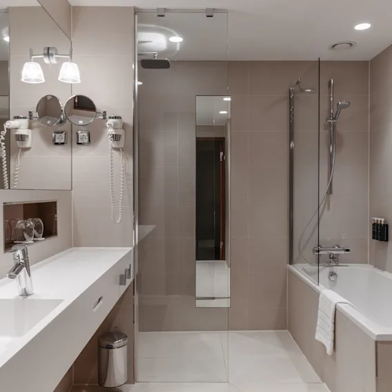 Modernt hotellbadrum med handfat, spegel, dusch och badkar. Toalettartiklar: Hand & Body Wash, Hand & Body Lotion.