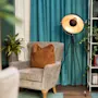 Lænestol med brun pude står i rum med blå gardiner. Lampe på stativ står ved siden af. Reol med bøger og dekorative genstande står i hjørnet. Frodig plante komplementerer det hyggelige opstilling.
