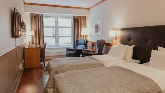 A cozy hotel room with two single beds, a desk, and a seating area by the window.