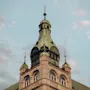 Historiallinen kivitorni pyöreine ikkunoineen ja vihertävä patinoitunut katto kohoaa pilvistä taivasta vasten, koristeltuna koristeellisilla torneilla ja yksityiskohtaisilla koristeilla.