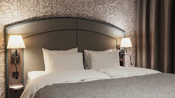 En bekväm hotellsäng med mjuk belysning, redo för en avkopplande vistelse.