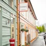 Bygning skilt med teksten "HAMMER HOME HOTEL" på en oransje bygning. Toetasjes bygninger langs en våt gate med parkerte biler. Trær synlige i bakgrunnen.