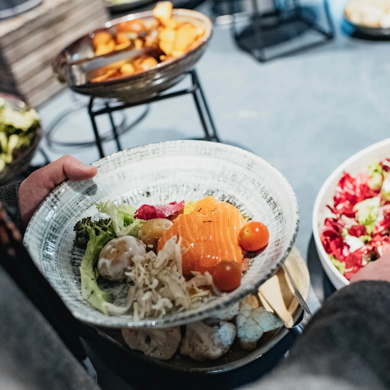 A person serving themselves a variety of fresh salad ingredients from a buffet.
