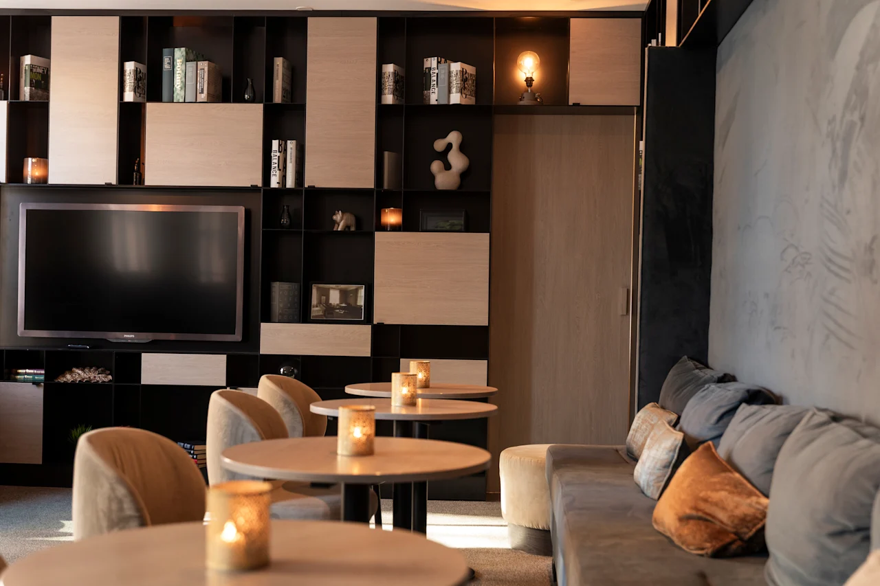 Et hyggeligt loungeområde med et stort tv, hylder fyldt med bøger, små borde med tændte stearinlys og en komfortabel sofa.