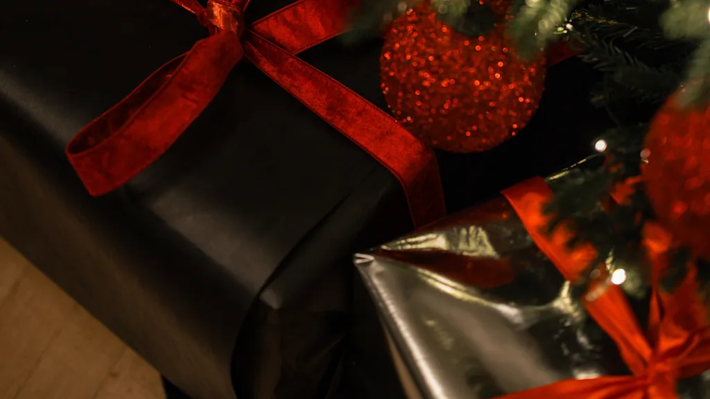 Wrapped gifts with red ribbons under a Christmas tree adorned with red ornaments and lights.