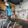 Treadmills and exercise machines in a gym with murals, including a blue figure and people lifting weights. Text: "MY ROCK & ROLL IS BETTER THAN YOUR BODYBUILDING BUT NOT EVERYBODY CAN PLAY THAT GOOD."