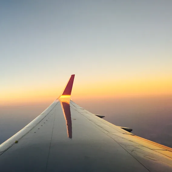 En flyvinge svever gjennom himmelen under en vakker solnedgang, med varme oransje og blå farger som maler horisonten.