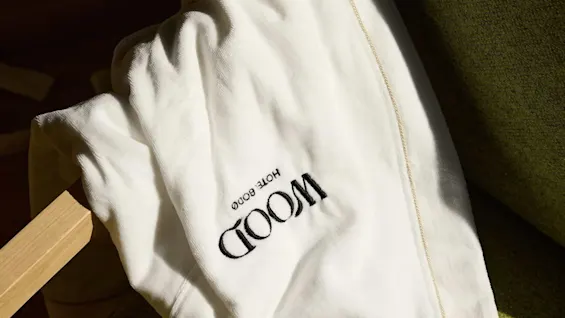 A white towel drapes over a green chair; sunlight casts shadows. Text on the towel reads "MOOD HOTEL GOOD."