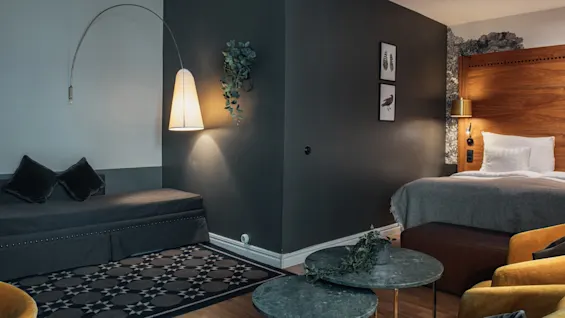 Et stilfuldt hotelværelse med en hyggelig seng, en komfortabel sofa og et lille siddeområde, alt i varme, indbydende toner.