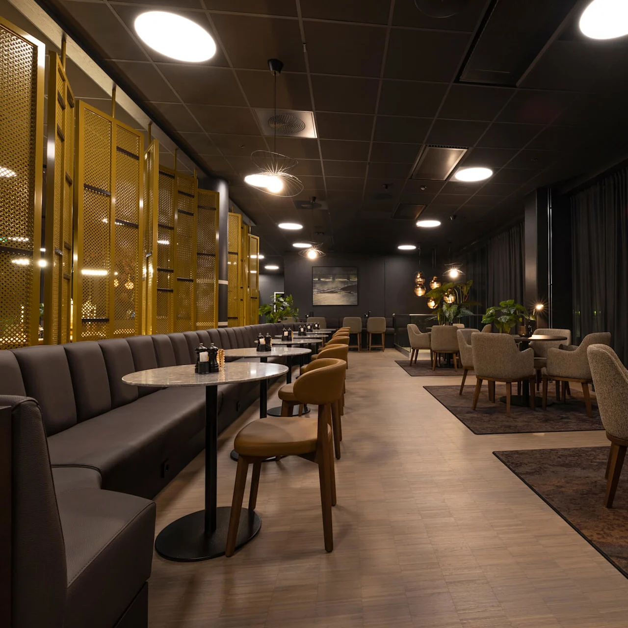 A modern restaurant interior with empty upholstered benches, chairs around tables, and ambient lighting.