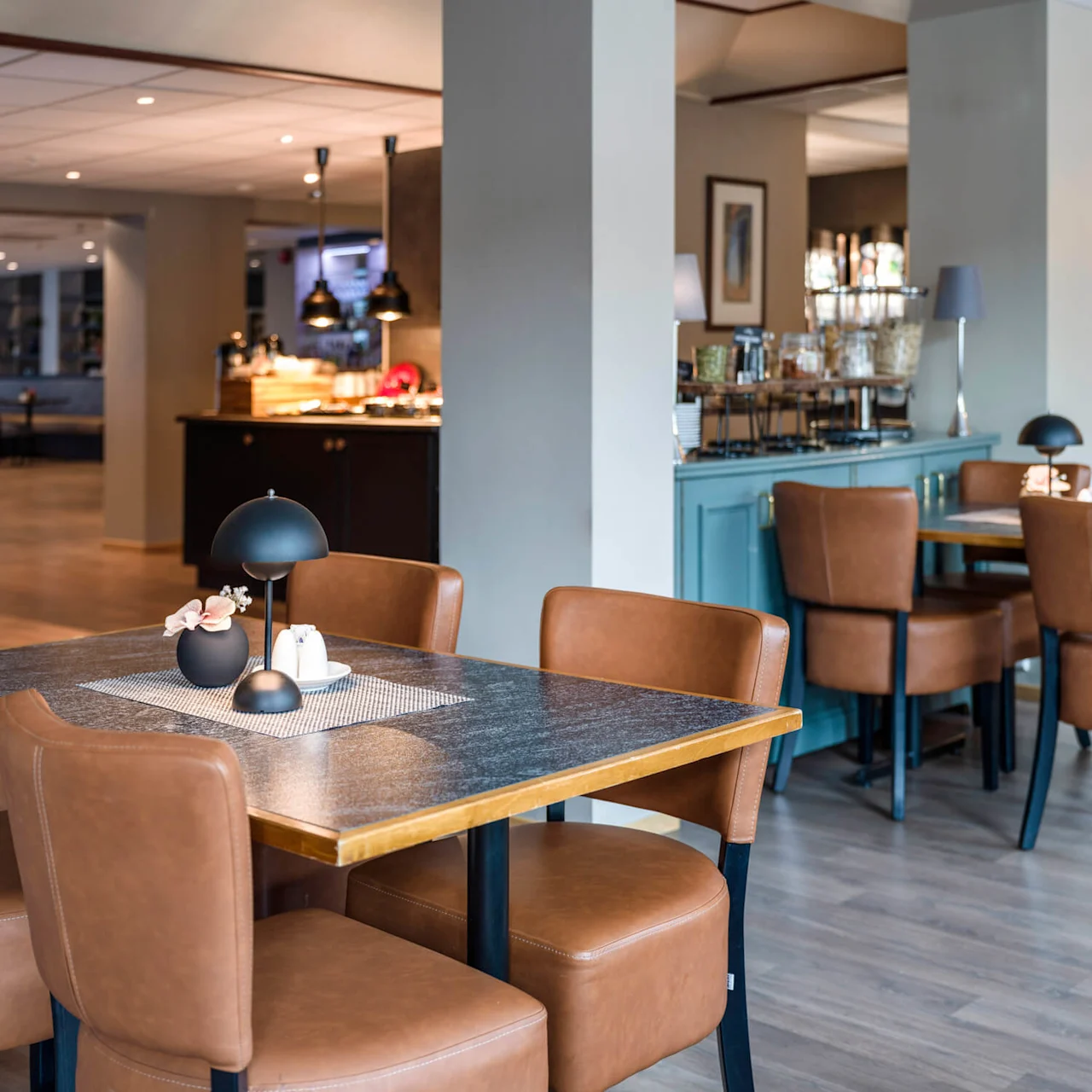 A wooden table with brown leather chairs sits in a modern restaurant, adorned with a black lamp, small vase, and salt and pepper shakers.