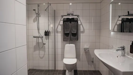 Ett rent och modernt badrum med en dusch, en toalett med rena handdukar och ett väl upplyst handfat.