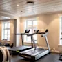 Tredemøller står ubrukte i et moderne treningsstudio, omgitt av treningsutstyr og belyst av naturlig lys gjennom store vinduer.