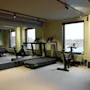 Ett modernt gym med löpband, en motionscykel och vikter, med stora speglar och fönster för en ljus träningsyta.