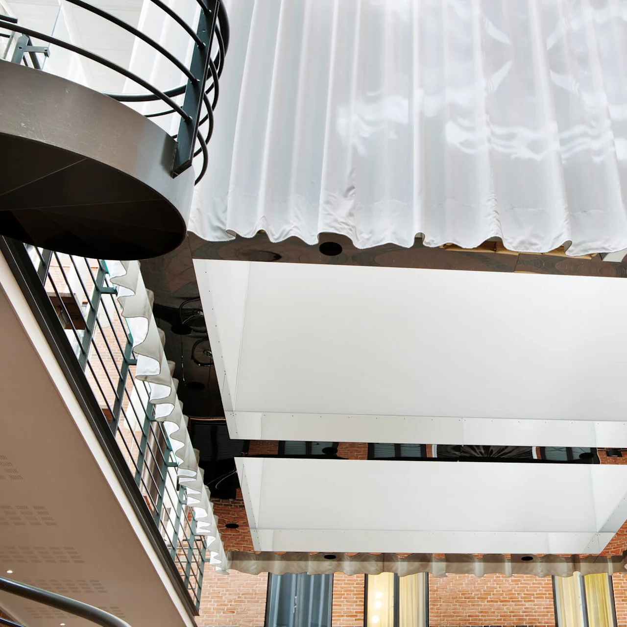 A modern atrium with white, wavy curtains hanging from the ceiling and reflective surfaces that enhance the lighting