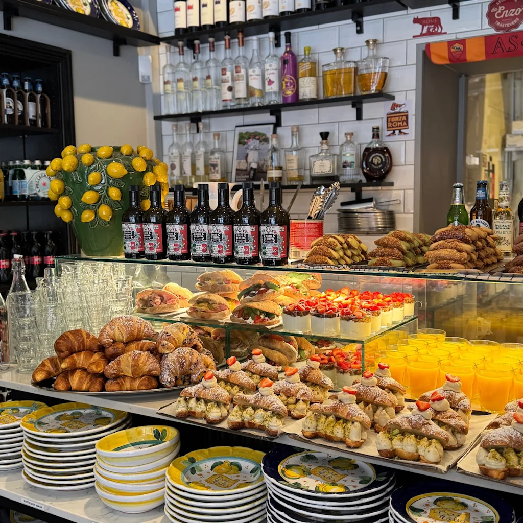 En livlig kafédisk med färska bakverk, smörgåsar och drycker. Dekorativa tallrikar visas, pris Mattallrik 299 KR, Assiette 349 KR.