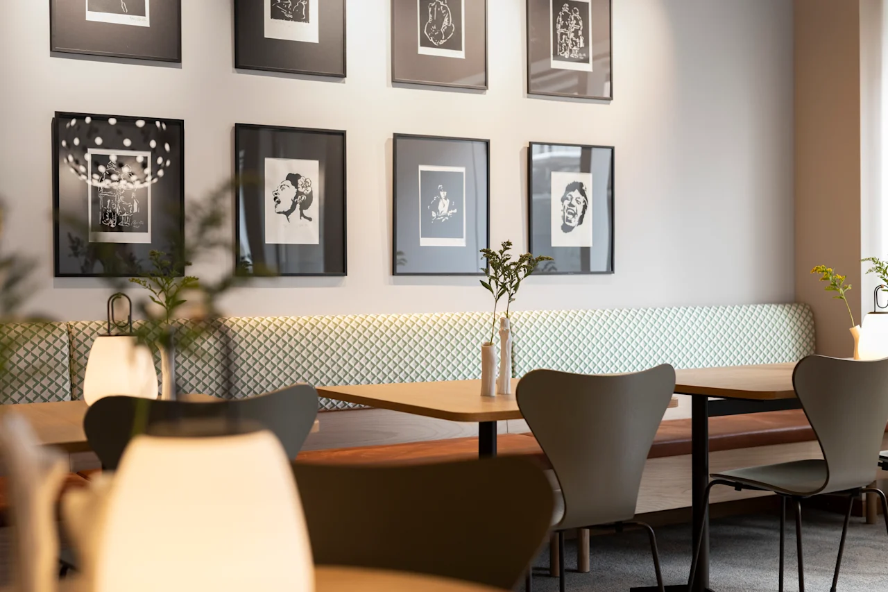Ett matutrymme med moderna stolar och bord med små växter, inramad konst på ljusa väggar och mjuk hängande belysning, vilket skapar en mysig, modern atmosfär.