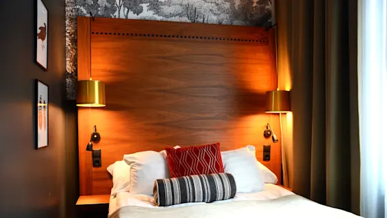 A neatly made bed with pillows and a wooden headboard, flanked by golden lamps, in a cozy room.