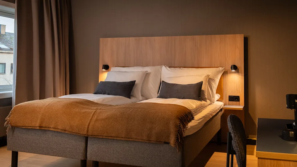 A cozy hotel room with two beds, warm lighting, and a window with curtains. An inviting space for rest and relaxation.