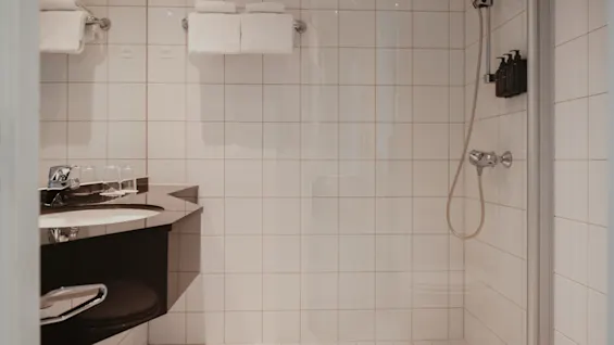 Ett rent, modernt badrum med handfat, spegel och duschutrymme, med vita kakelplattor och fräscha handdukar.