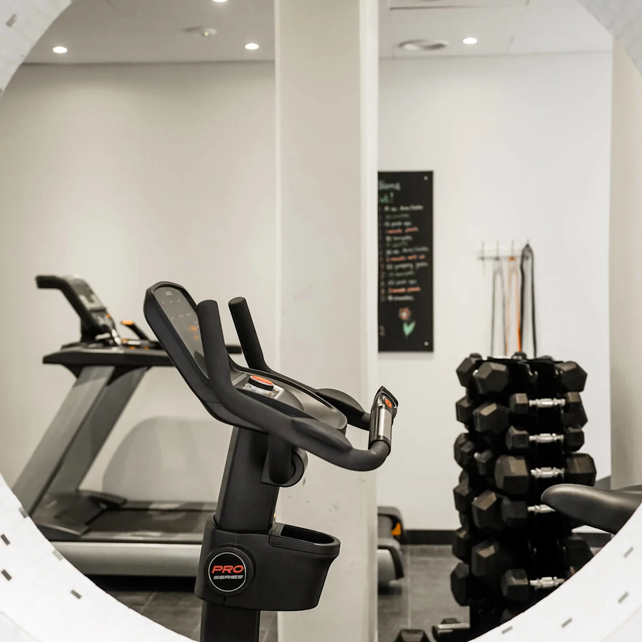 Löpband står stilla i ett gym, omgivet av en hantelställning och motståndsband på en vägg i ett väl upplyst, modernt träningsrum.