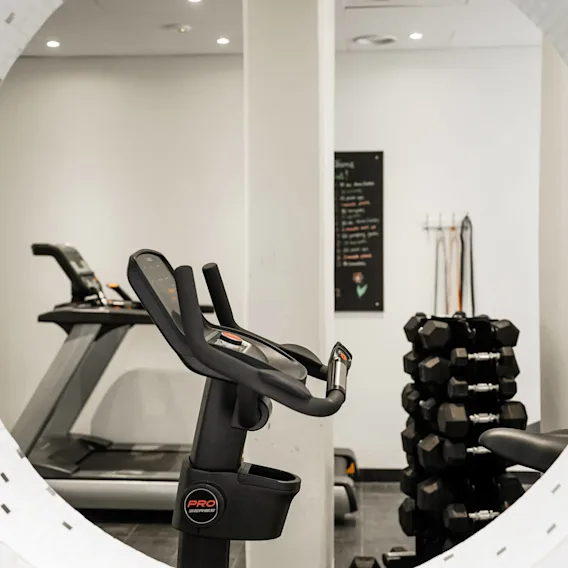 Löpband står stilla i ett gym, omgivet av en hantelställning och motståndsband på en vägg i ett väl upplyst, modernt träningsrum.