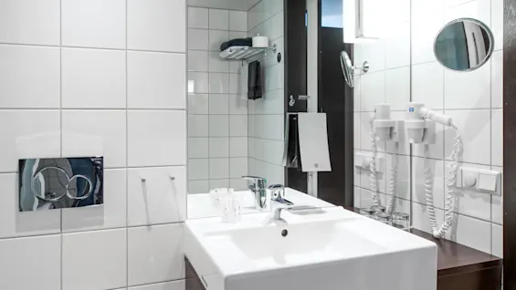 Et moderne bad med en hvit vask montert på en mørk trebenk. Et speil reflekterer rommet og viser flislagte vegger og et håndkleholder.