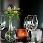 Et vakkert dekket bord med en vase med blomster, et glødende lys og glitrende glass, klart for et måltid.