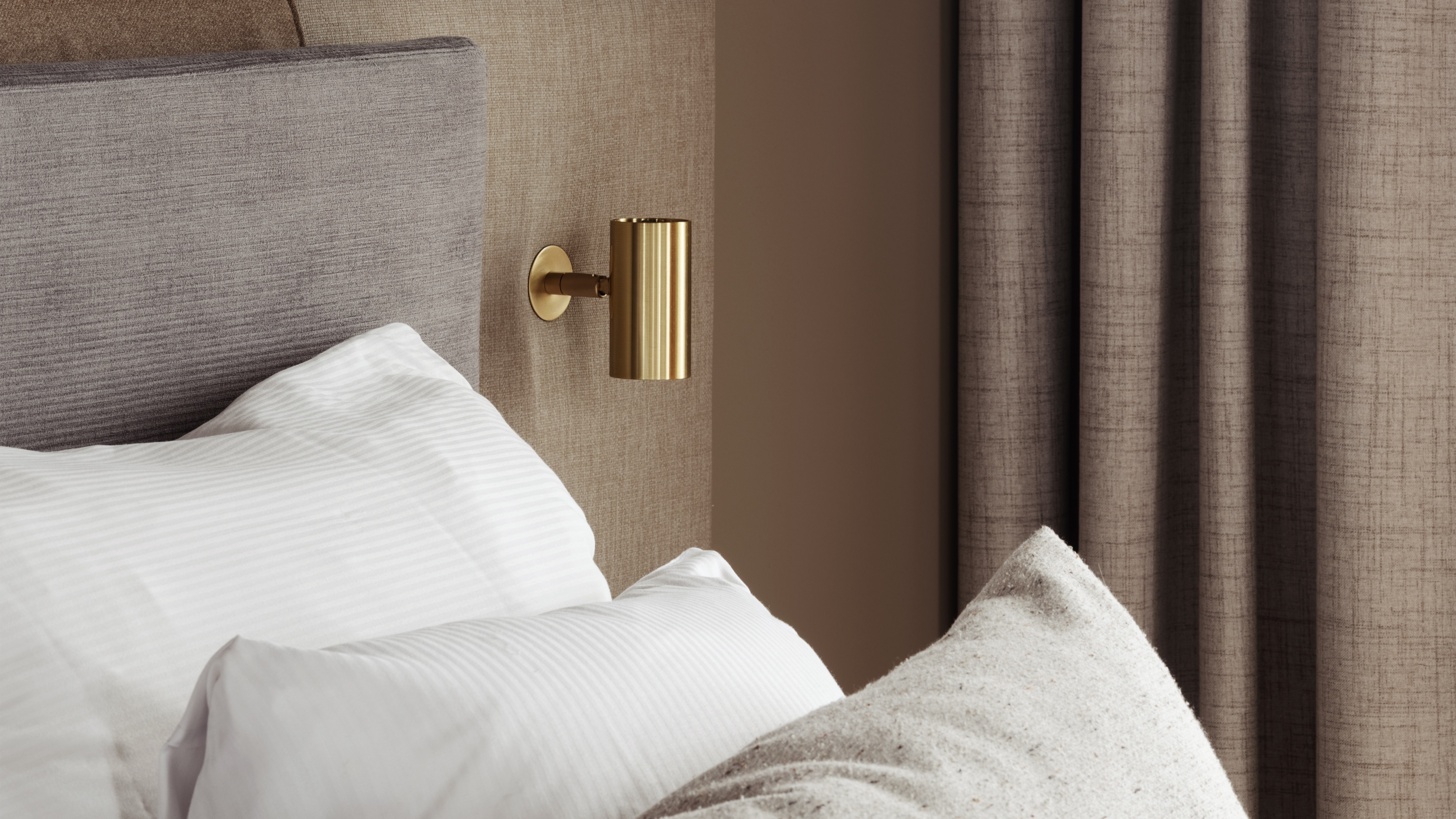 Ett mysigt sovrum med en säng, kuddar och varm belysning från en hängande sfärisk lampa och en väggmonterad lampa. Gardiner är fördragna.