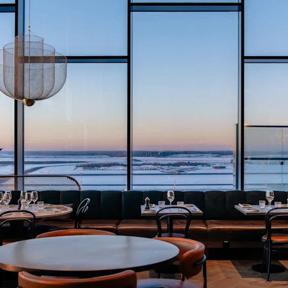 Ravintola NÒR Clarion Hotel Helsinki Airportissa, katetut pöydät ja lumimaisemanäkymä hämärässä.