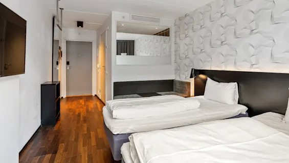 A modern hotel room with patterned wallpaper, two beds, and wooden flooring.