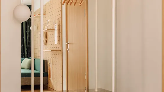 A modern entryway at hobo oslo featuring a white clothing rack, a bench, and red slippers on a checkered floor.