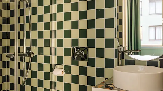 A modern bathroom with green and light green checkered tiles, featuring a shower, toilet, and sink with a mirror.