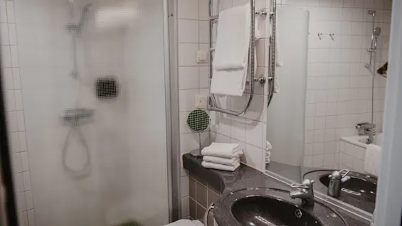 Siisti ja toimiva hotellin kylpyhuone Home Hotel Uppsalassa, jossa on suihku, wc ja pesuallas puhtailla pyyhkeillä.