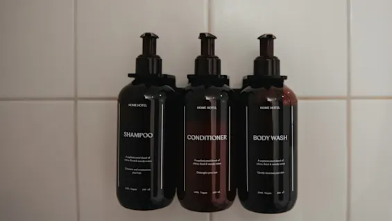 Three dark bottles of shampoo, conditioner, and body wash from Home Hotel Uppsala mounted on a tiled wall, ready for use.