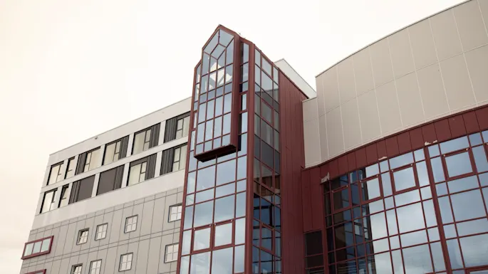 A modern architectural building with a large, multi-story glass section extending outwards, complemented by red and grey panels.