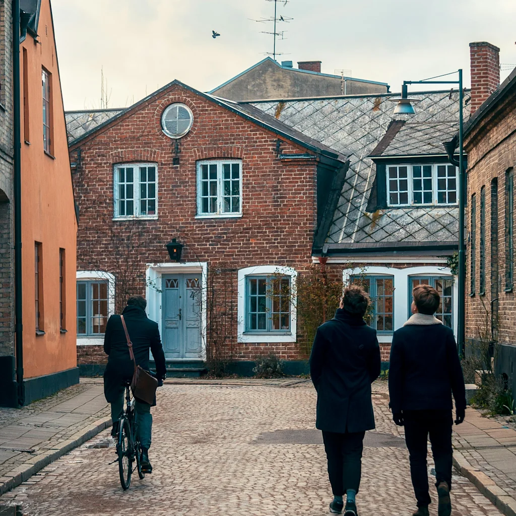 Folk sykler og går på en sjarmerende brosteinsgate i Lund, omgitt av historiske mursteinsbygninger.
