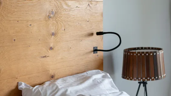 Et hyggeligt soveværelse med sengegavl i træ, hvide og grønne puder samt en stilfuld sengelampe.