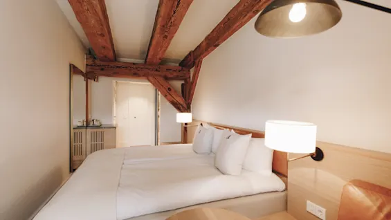 Ett mysigt hotellrum med en bekväm säng, synliga takbjälkar i trä och varm belysning.