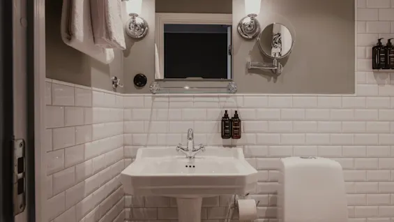 A clean, modern bathroom with white subway tiles, a pedestal sink, mirror, and toilet. Home Hotel Baltzar - Compact Single.